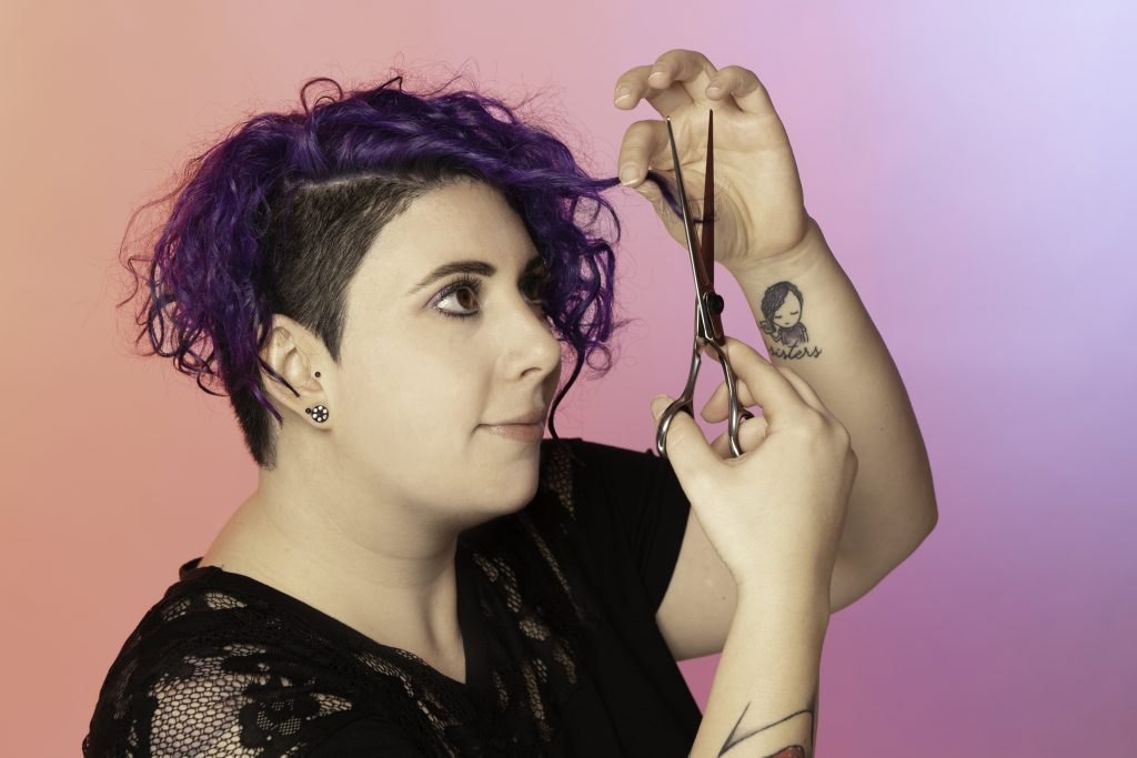 Maria Martin mit violetten Haaren hält eine Friseurschere